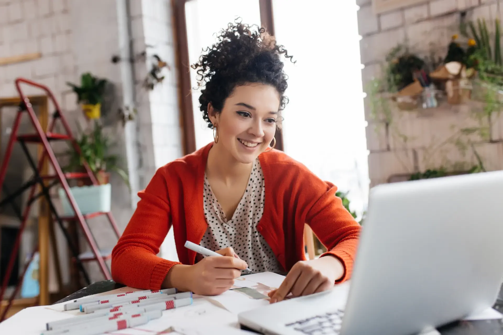 Mulher estudando inglês para executivos, sorrindo e fazendo anotações enquanto acompanha uma aula online.