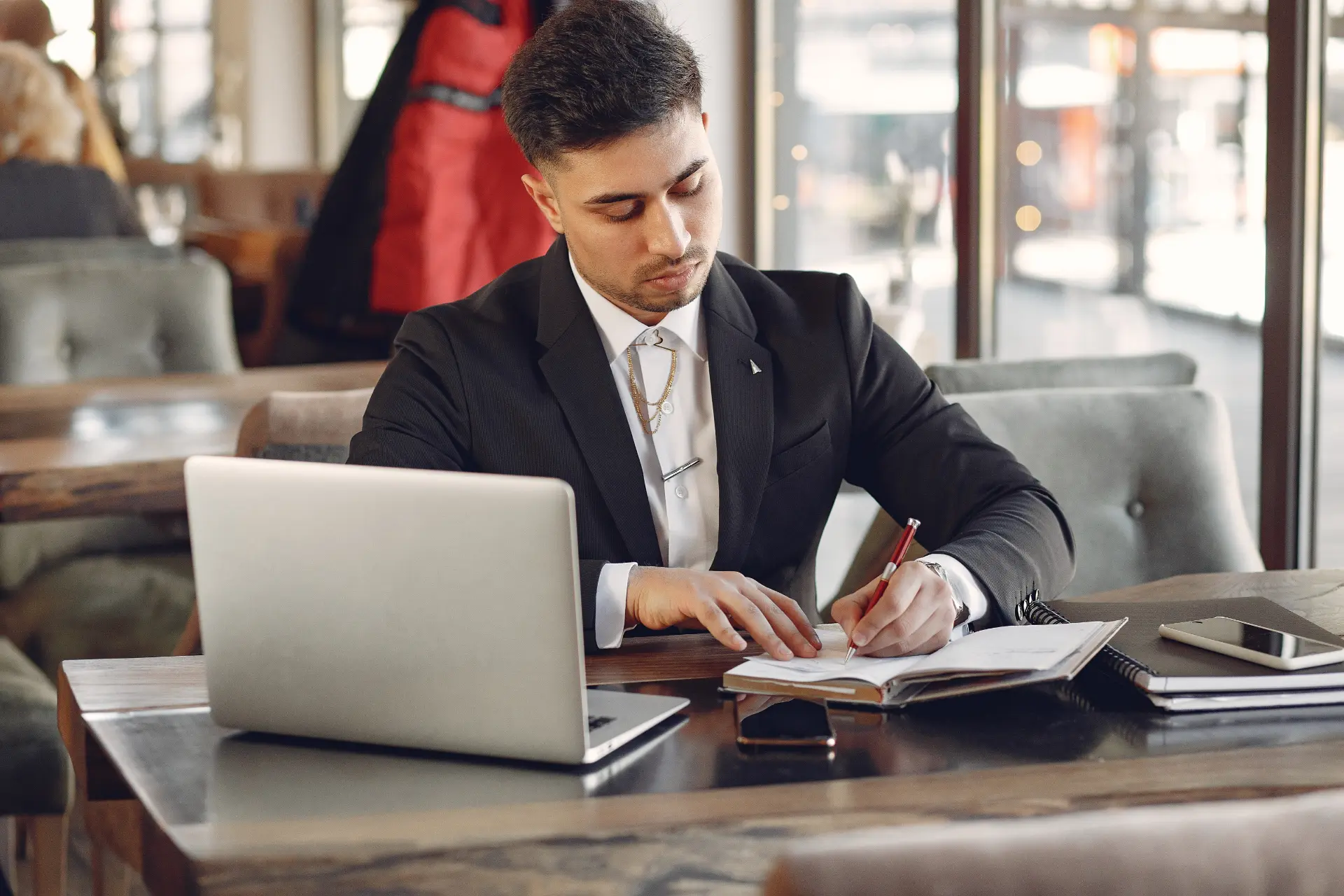 Jovem empresário elegante em um café, estudando com um caderno e laptop, focado em seu treino de inglês diário.